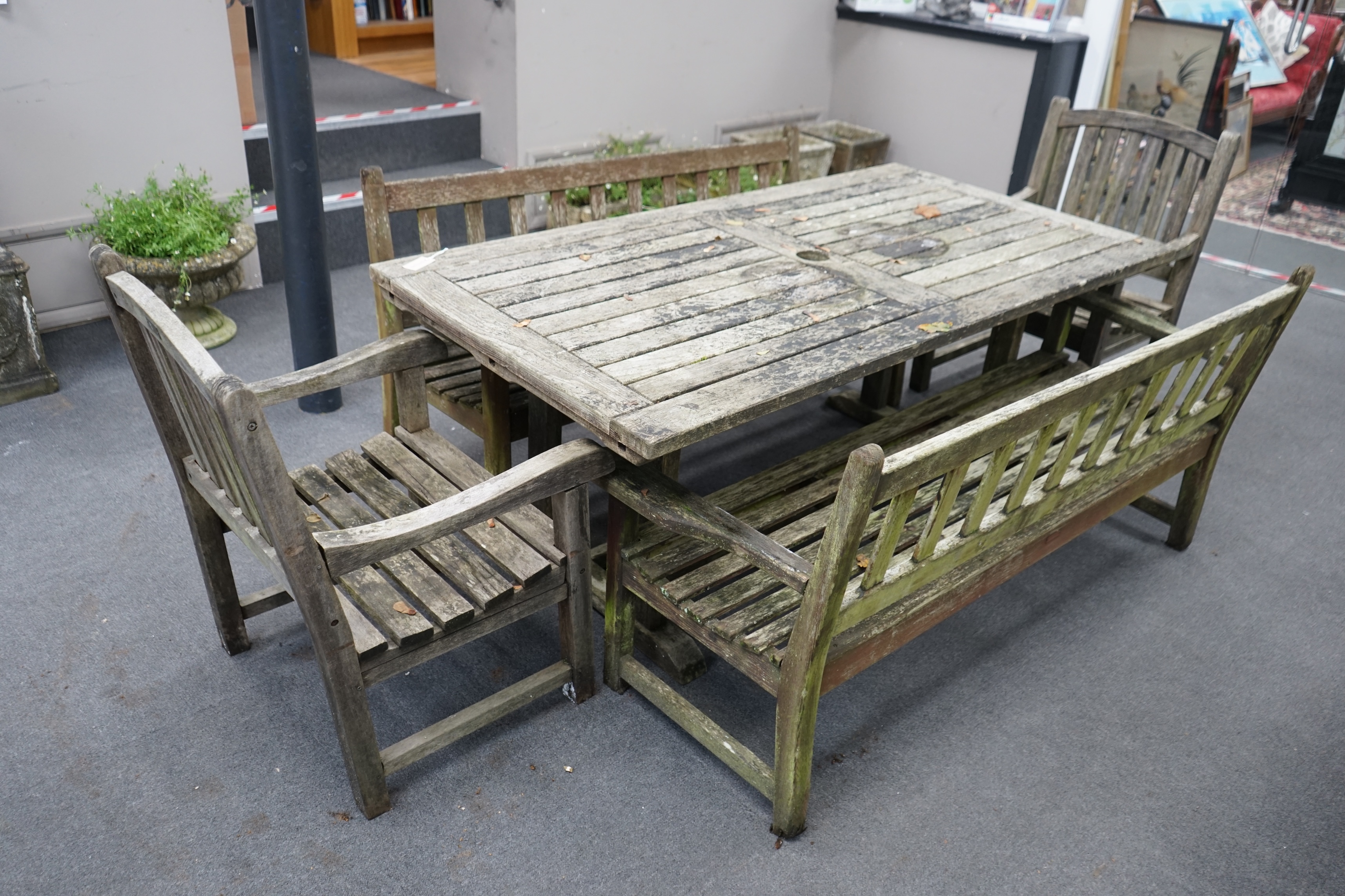 A weathered teak extending garden table, with pair of matching slatted benches and two elbow chairs